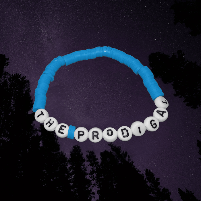 Blue and white beaded bracelet with 'THE PRODIGAL' text against a dark forest background